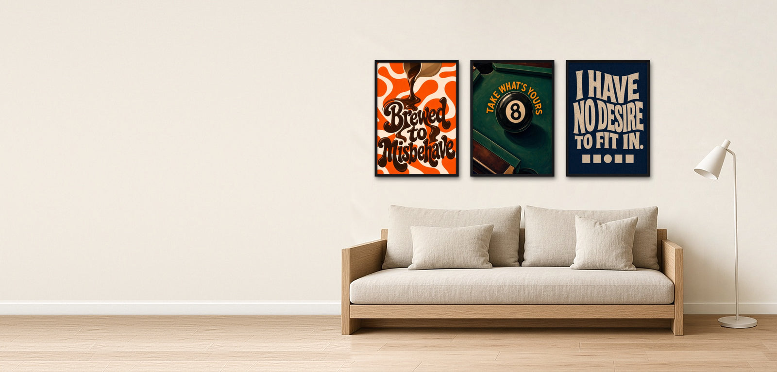 Brewed to Misbehave, Take What's Yours and I Have No Desire To Fit In in black frames on a warm white wall, above a linen sofa with a white floor lamp beside it